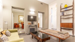 A modern living room with a sofa, a glass-top coffee table, a fireplace, a television, and a bookshelf.