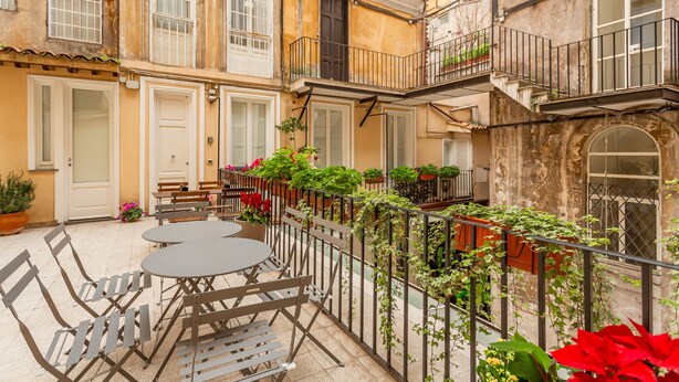 A courtyard with outdoor seating, potted plants, and a building facade with multiple windows and balconies.