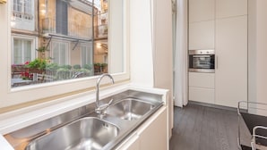A modern kitchen with a stainless steel sink, a built-in oven, and a window overlooking a courtyard with plants and a balcony.