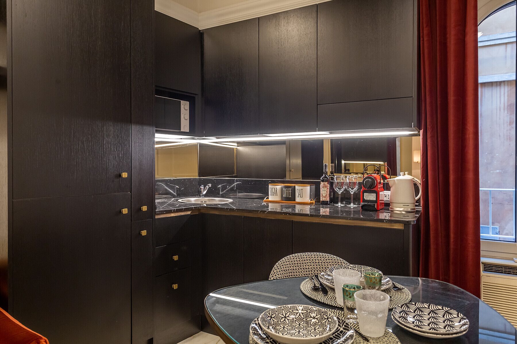 A modern kitchen with dark cabinetry, a marble countertop, and a dining area with patterned tableware.