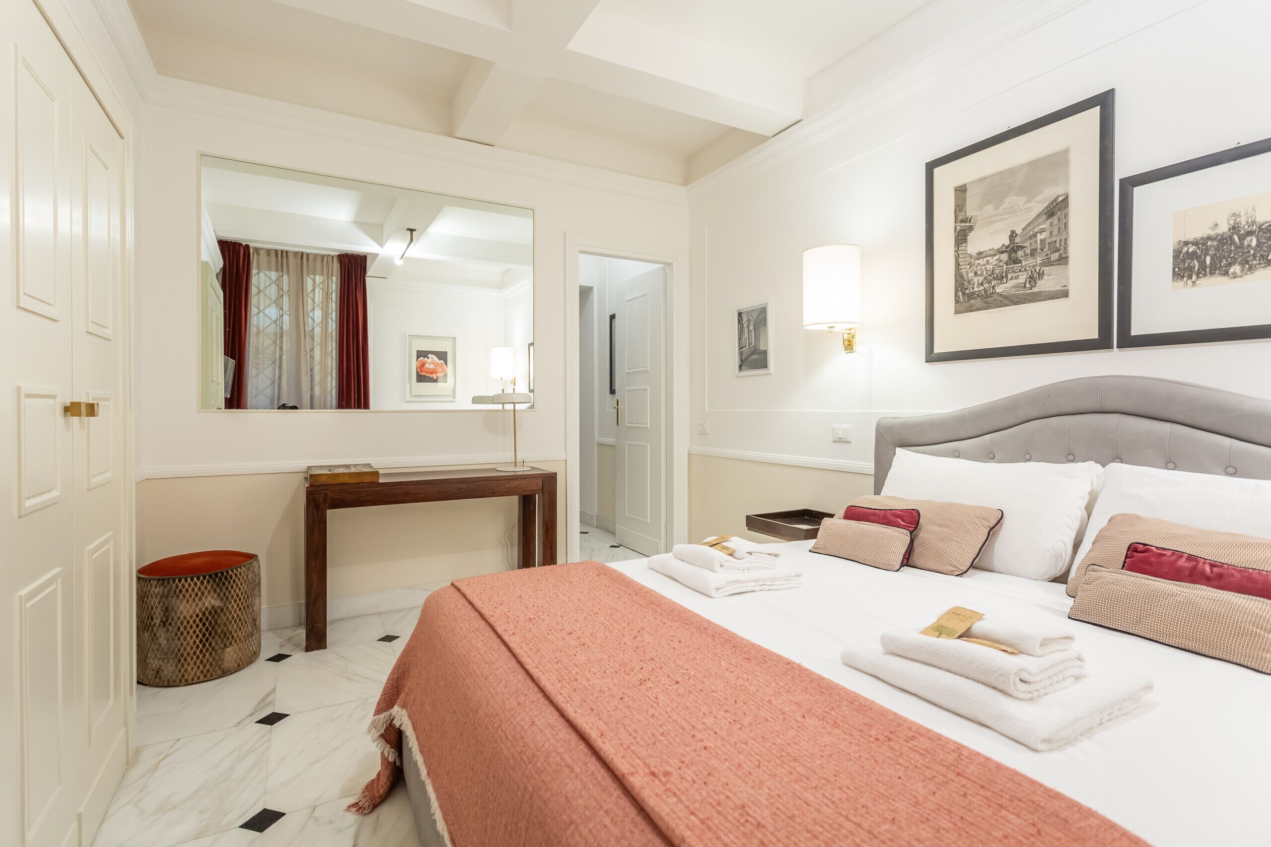 A hotel room with a bed, a desk, a mirror, and framed pictures on the wall.