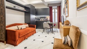En moderne stue med en sofa, et spisebord med stole, et køkken i baggrunden og en dekorativ buste på et bord.