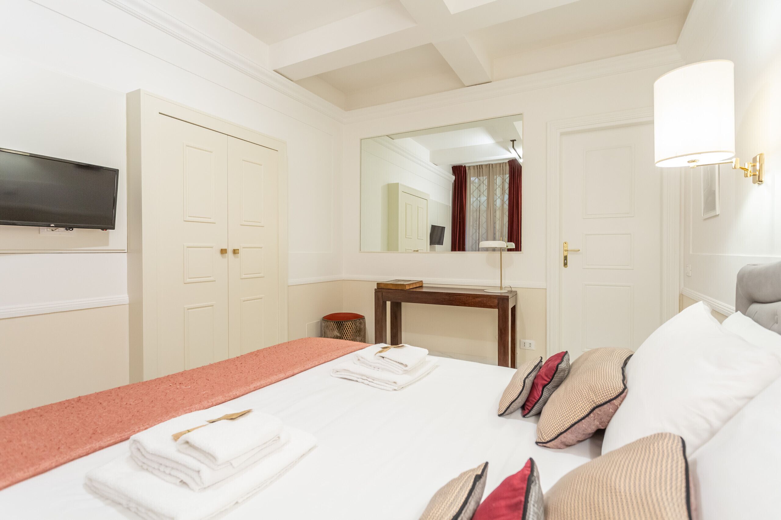 A hotel room with a bed, a TV, a mirror, a desk, and a lamp.