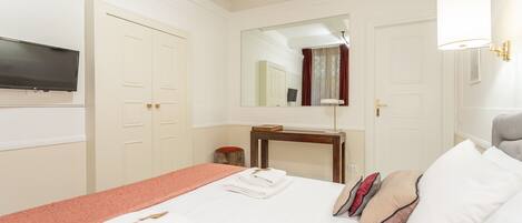 A hotel room with a bed, a TV, a mirror, a desk, and a lamp.