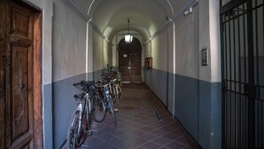 Ein Korridor mit Fahrrädern auf der linken Seite, einer Holztür und einem Metallgitter auf der rechten Seite.