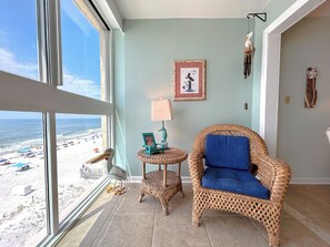 Una habitación con un gran ventanal con vista a la playa, muebles de mimbre, un cuadro enmarcado y una lámpara.