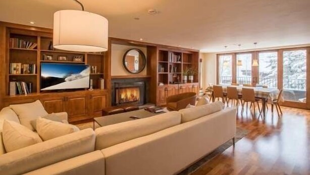 A spacious living room with a fireplace, bookshelves, a large TV, and a dining area with natural light from large windows. - Northwoods Private Condo with Easy Ski-In Ski-Out Access by RedAwning (Vail)