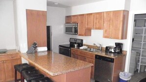 A compact kitchen with wooden cabinets, a central island with stools, a microwave, a refrigerator, and a coffee maker. - 17 Vail Road Condos Short Walk to Vail Village and Gondola One by RedAwning (Vail)