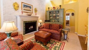 Una sala de estar acogedora con chimenea, muebles con diseños y un mueble verde decorado con objetos.