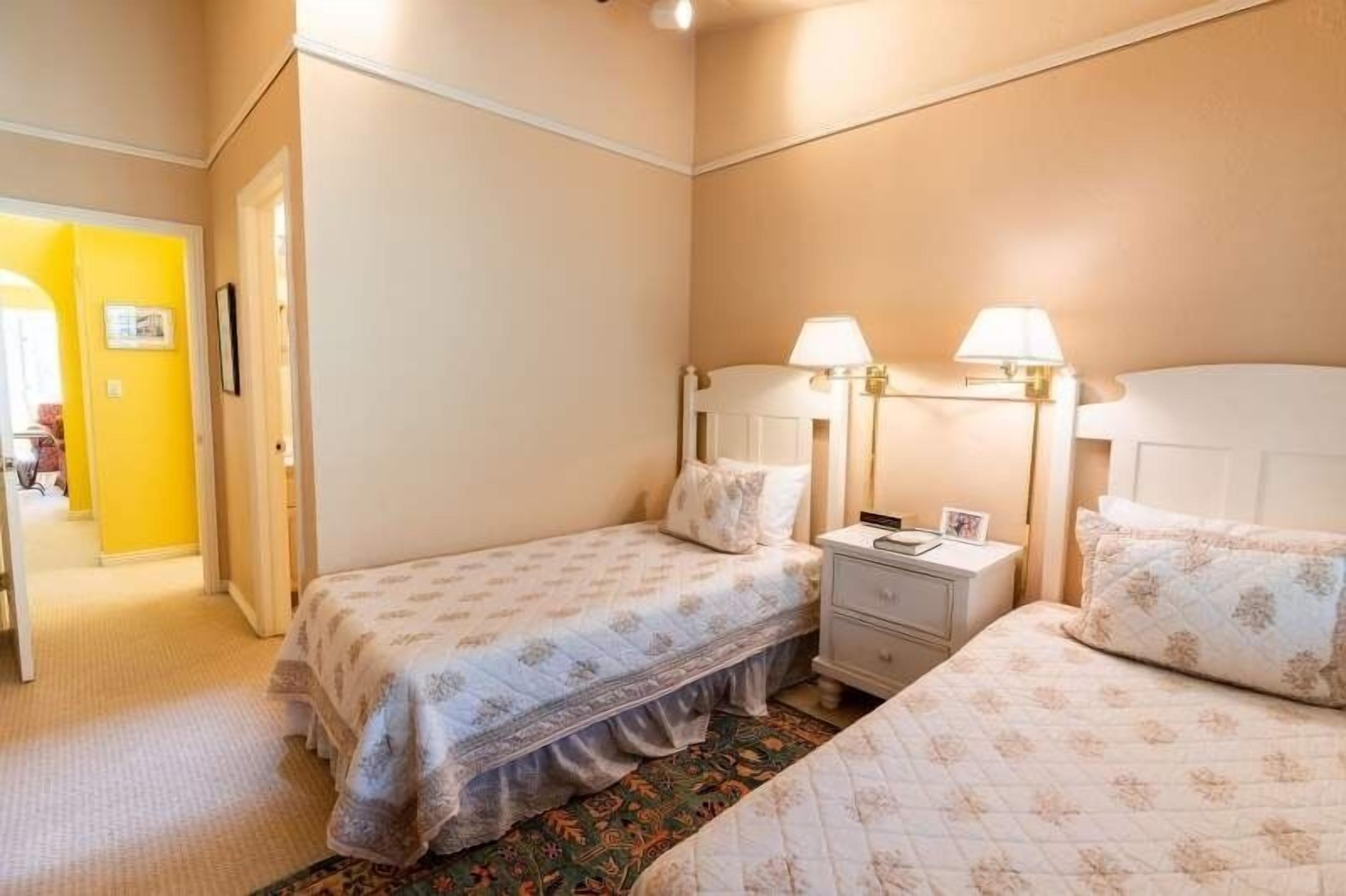A hotel room with two beds, a nightstand, and a lamp.