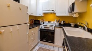 Una cocina compacta con gabinetes blancos, estufa, microondas y fregadero.
