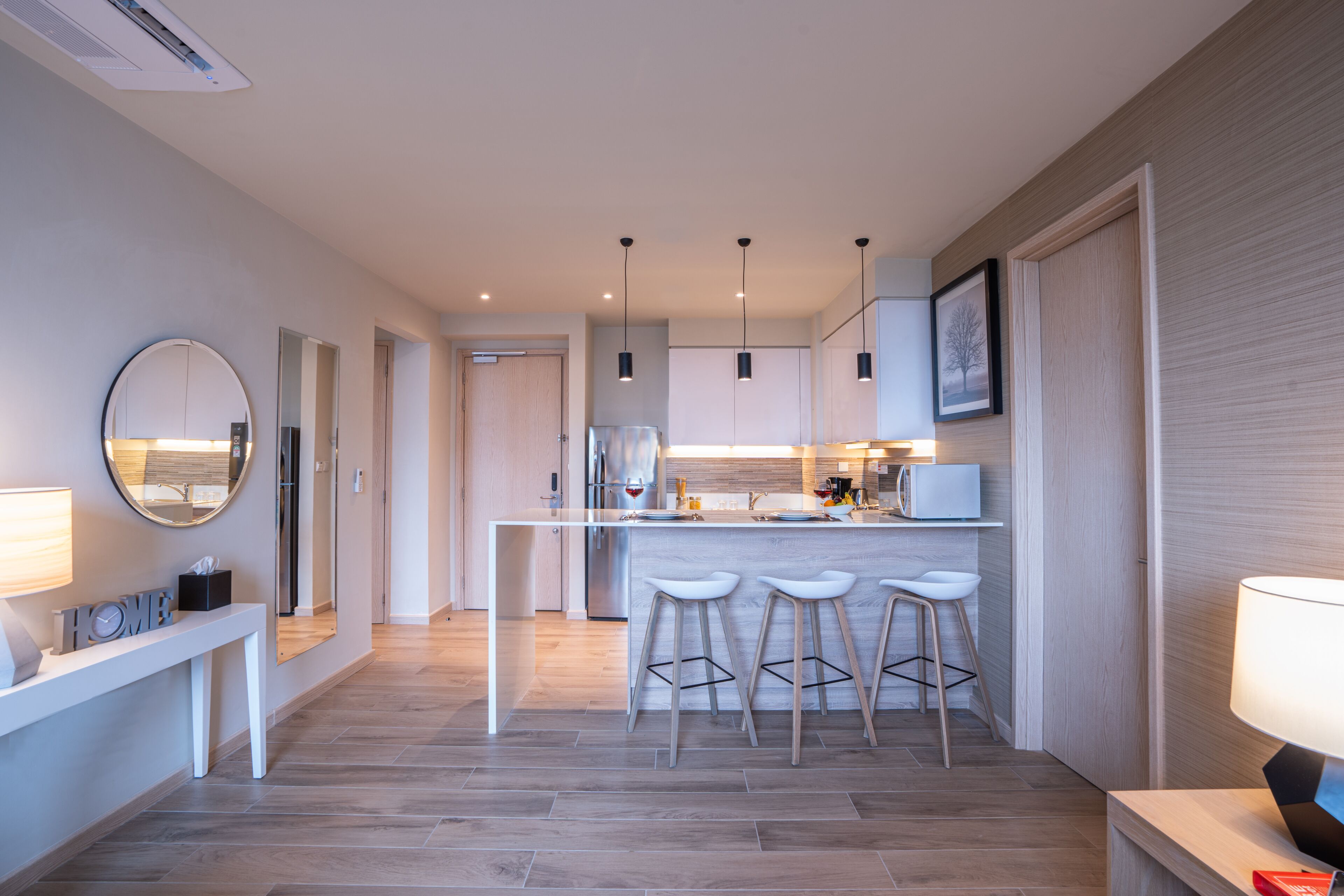 A modern kitchen with a central island, bar stools, pendant lights, and a large mirror.