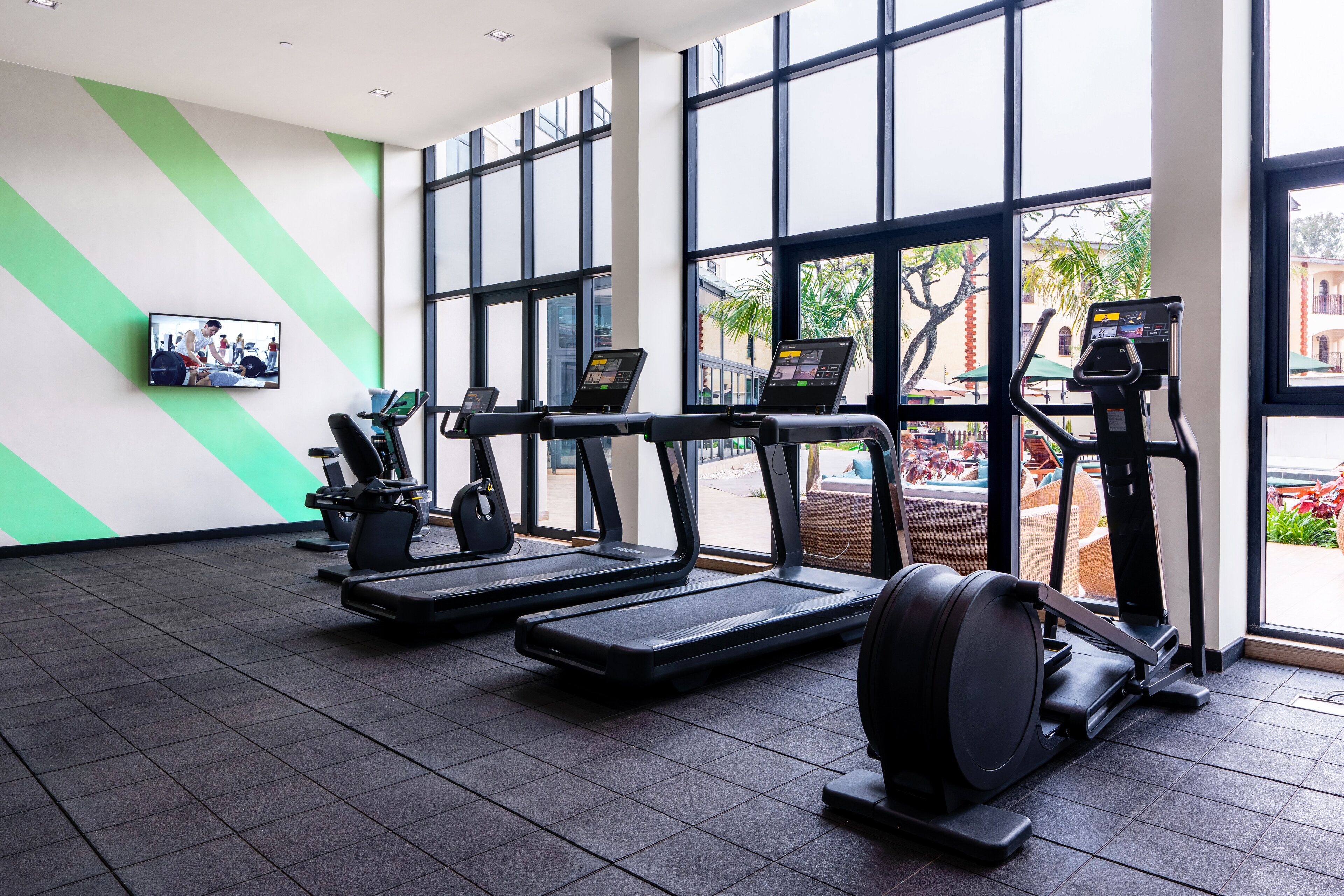 Ein Fitnessstudio mit Laufbändern, Crosstrainern und einem stationären Fahrrad.