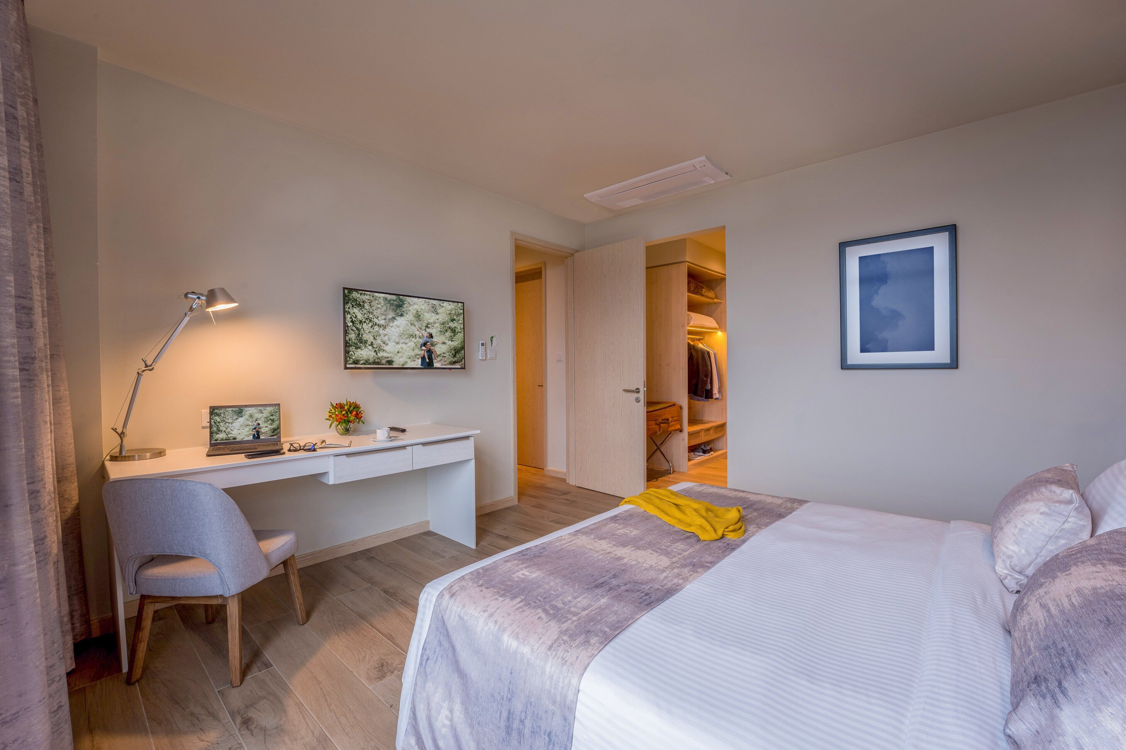 Un dormitorio con cama, escritorio y silla. Hay un armario con ropa y una puerta que da a otra habitación.