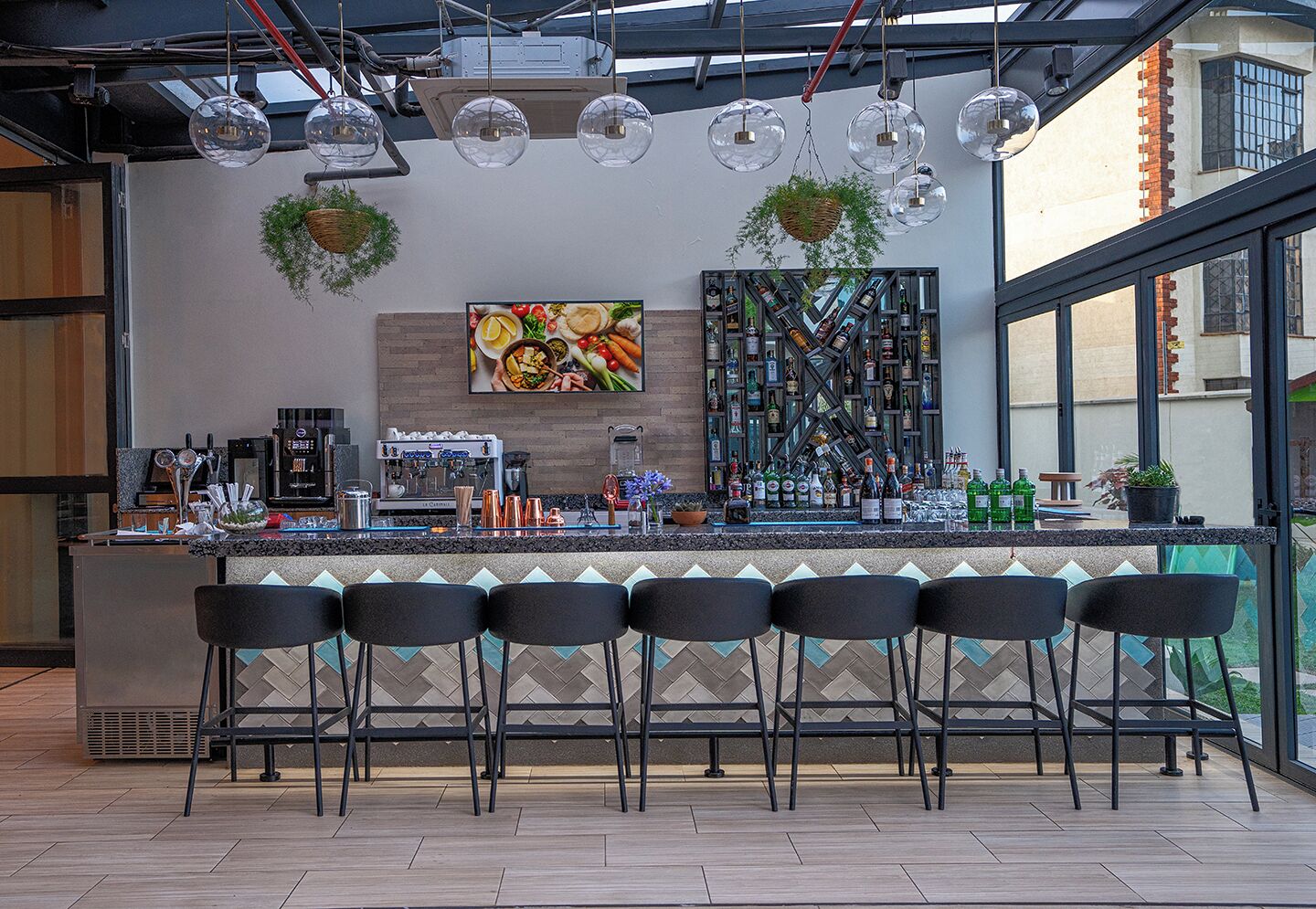A bar area with a counter, multiple stools, hanging spherical lights, a wall-mounted beverage display, and a large window.