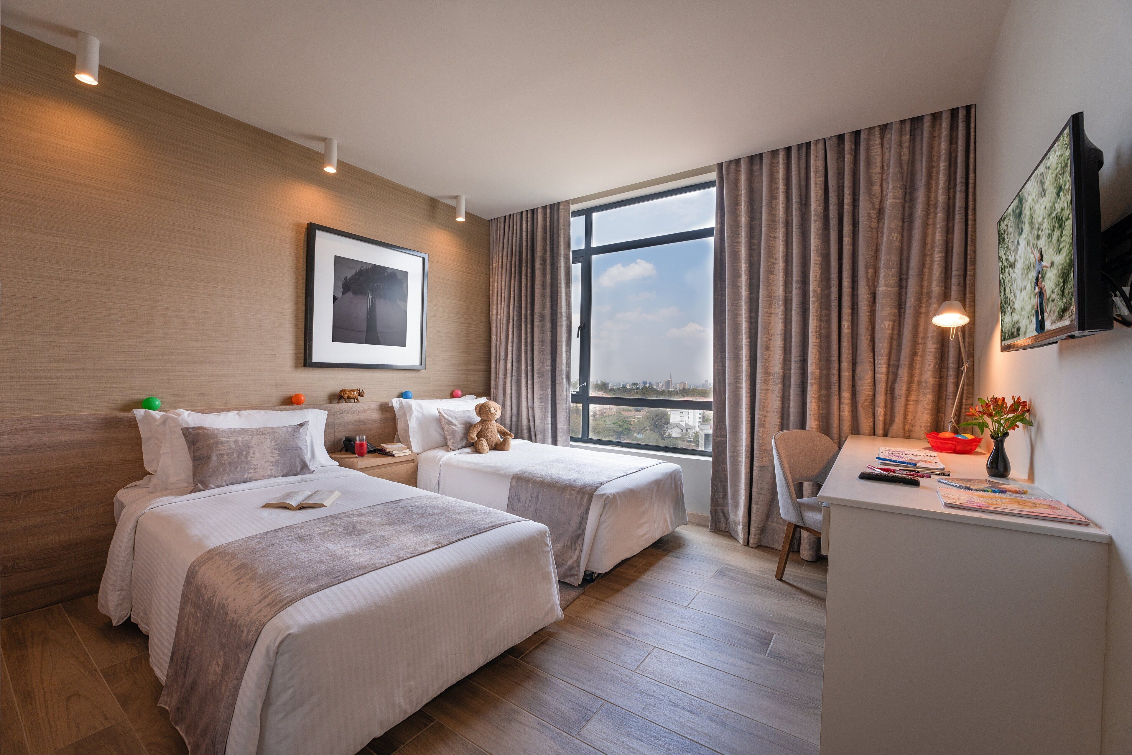 A hotel room with two beds, a desk, a chair, a TV, and a window with curtains.