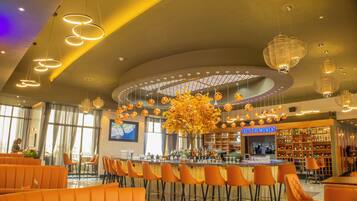 Zona de bar moderna con asientos naranja, una barra central y un arreglo de plantas decorativo.