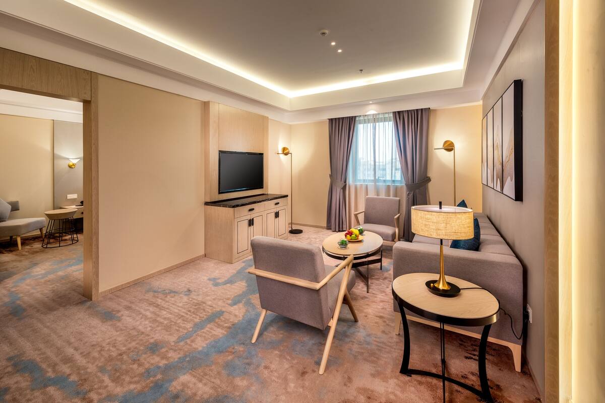 Ein modernes Hotelzimmer mit Flachbildfernseher, einer Couch, einem Esstisch und einer Lampe.