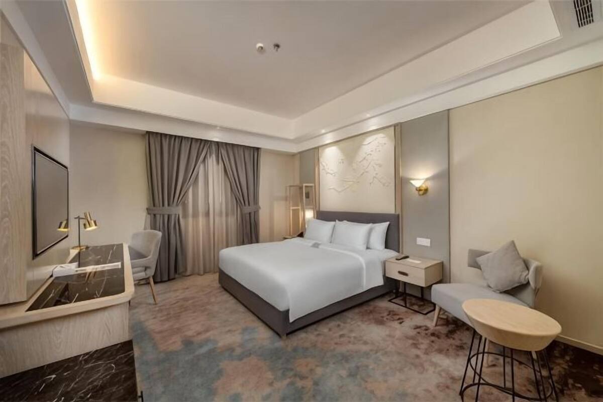 Ein modernes Hotelzimmer mit einem großen Bett, Nachttischen, einem Schreibtisch, einem Sessel und einem kleinen runden Tisch.