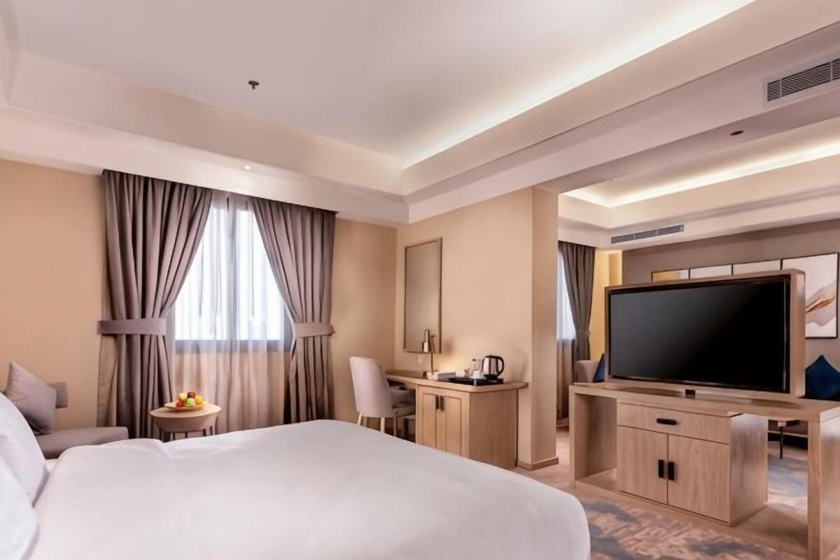 A hotel room with a large bed, a desk with a chair, a television, and a small table with a fruit bowl.