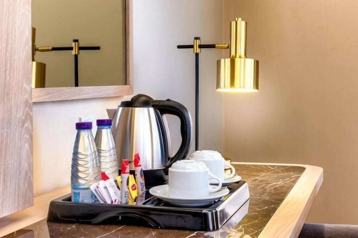 Ein Hotelzimmer mit Marmorplatte, einer Kaffeemaschine, zwei Tassen, einem Tablett mit Flaschen und einem Wasserkocher, sowie einer goldenen Pendelleuchte.