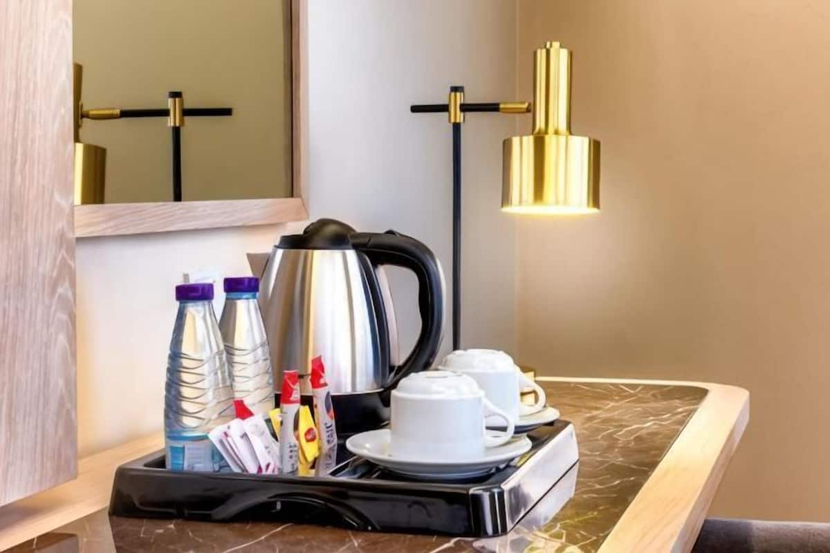 A hotel room with a marble countertop, a coffee maker, two cups, a tray with bottles and a kettle, and a gold pendant light.