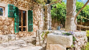 A stone building with green shutters, a stone staircase, and a tree in the background.