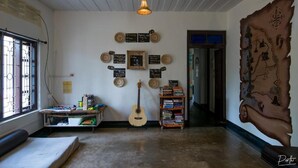 A room with a guitar, a bookshelf, a map on the wall, and a window with bars. - Piggy Hostel Varkala (Varkala)