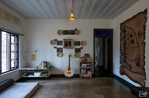 Una habitación con una guitarra, una estantería, un mapa en la pared y una ventana con barrotes.