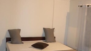 A single bed with a wooden frame, a ceiling fan, and a window with curtains. - Piggy Hostel Varkala (Varkala)