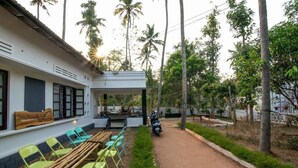 A rustic outdoor seating area with wooden and metal chairs, a motorcycle parked nearby, and a sign reading "SHORT CATCH HUNTERS". - Piggy Hostel Varkala (Varkala)