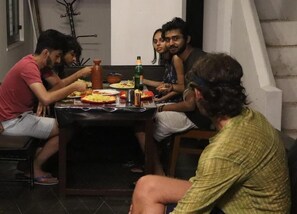 A group of people sitting around a table with food and drinks, in a room with a tiled floor and a simple, functional design.