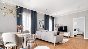 A modern living room with a sofa, dining table, and chairs. There is a TV and a white cabinet in the background. - Apartamenty Swinoujscie - Villa 44 (Swinoujscie)