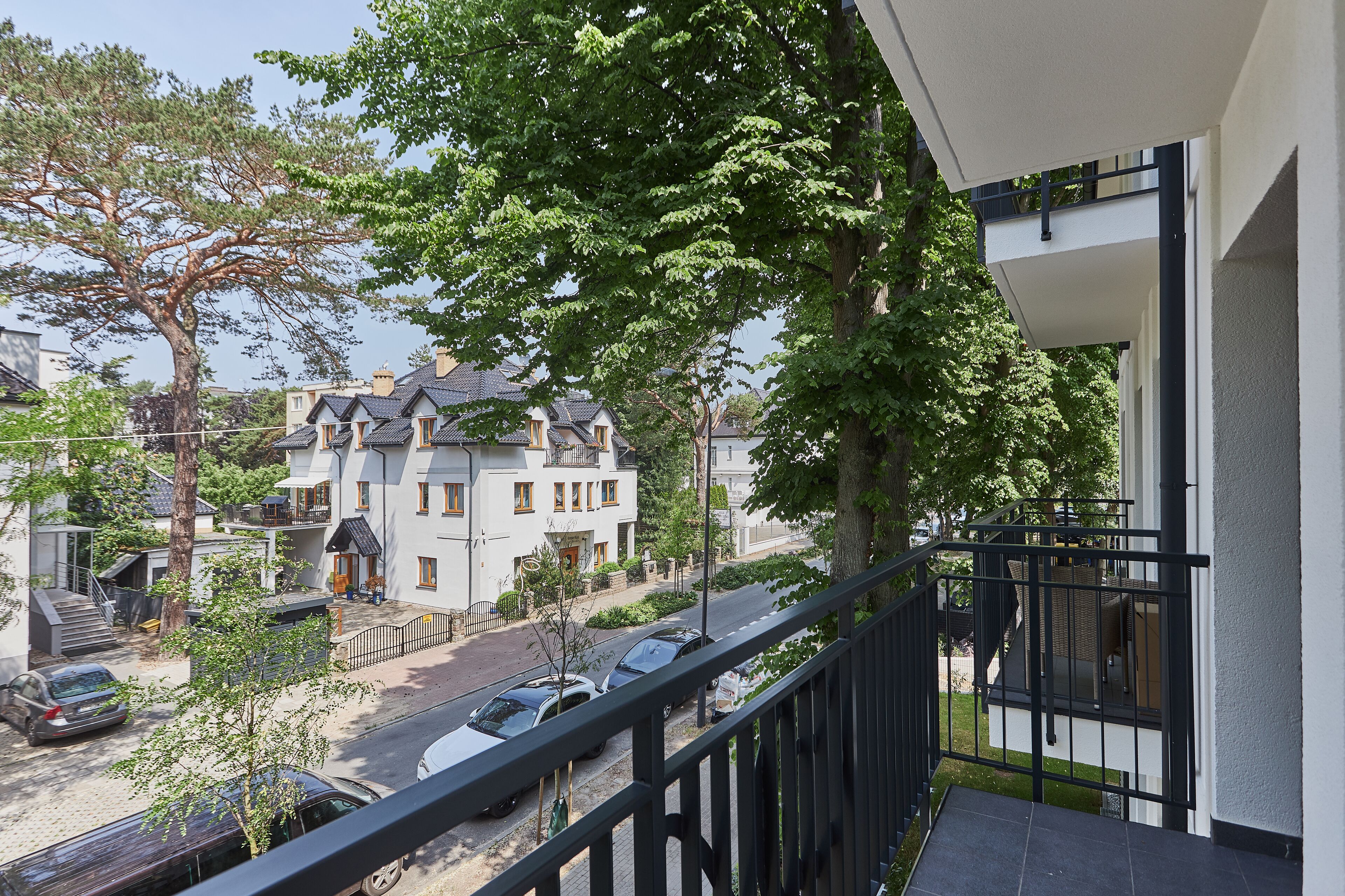 A residential building with a balcony, a tree in front, and parked cars on the street.