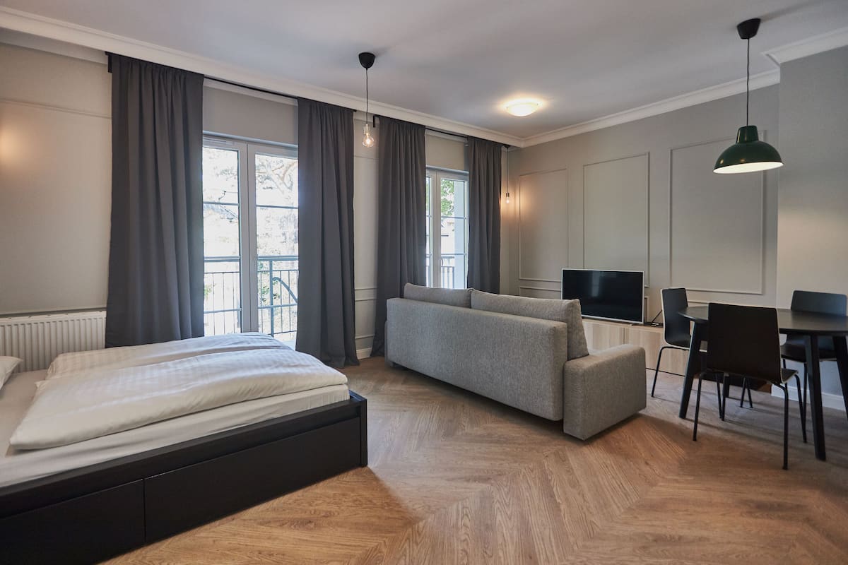 A modern hotel room with a bed, a sofa, a TV, and a dining area.