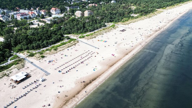 An aerial view of a beach with rows of beach chairs and umbrellas, a boardwalk, and buildings in the background. - Apartamenty Swinoujscie - Villa 44 (Swinoujscie)