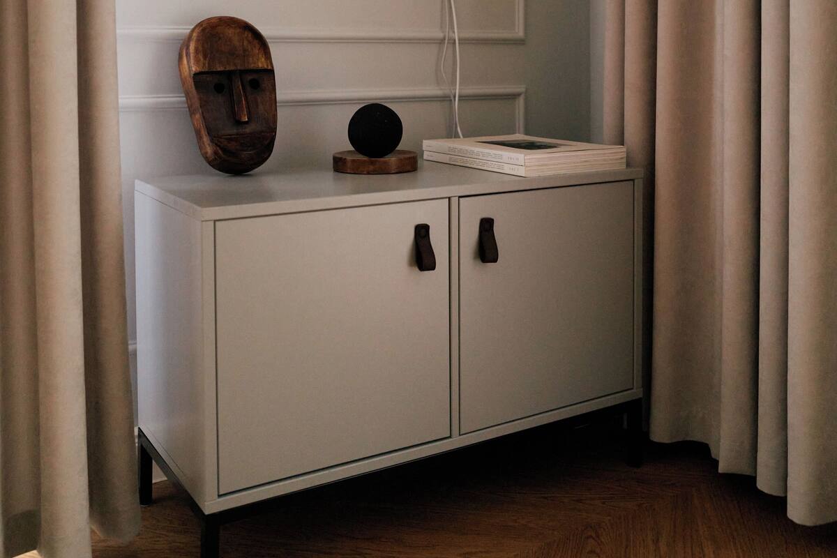 A modern room with a flat-screen TV mounted on the wall, a wooden mask on a white cabinet, and a small round object on top.