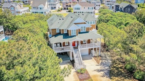 Et kystnære boligområde med flere huse, et fremtrædende hus med balkon og garage, omgivet af tætte træer og frit vue over havet.