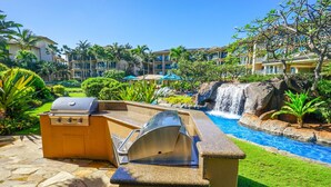 Zona de piscina exterior con cascada, una parrilla y un área de descanso junto a la piscina.