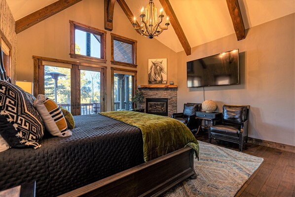 A spacious bedroom with a large bed, a fireplace, a TV, and a balcony with large windows.