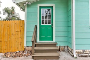 A green door with a window, a wooden fence, and a set of stairs leading to a house.