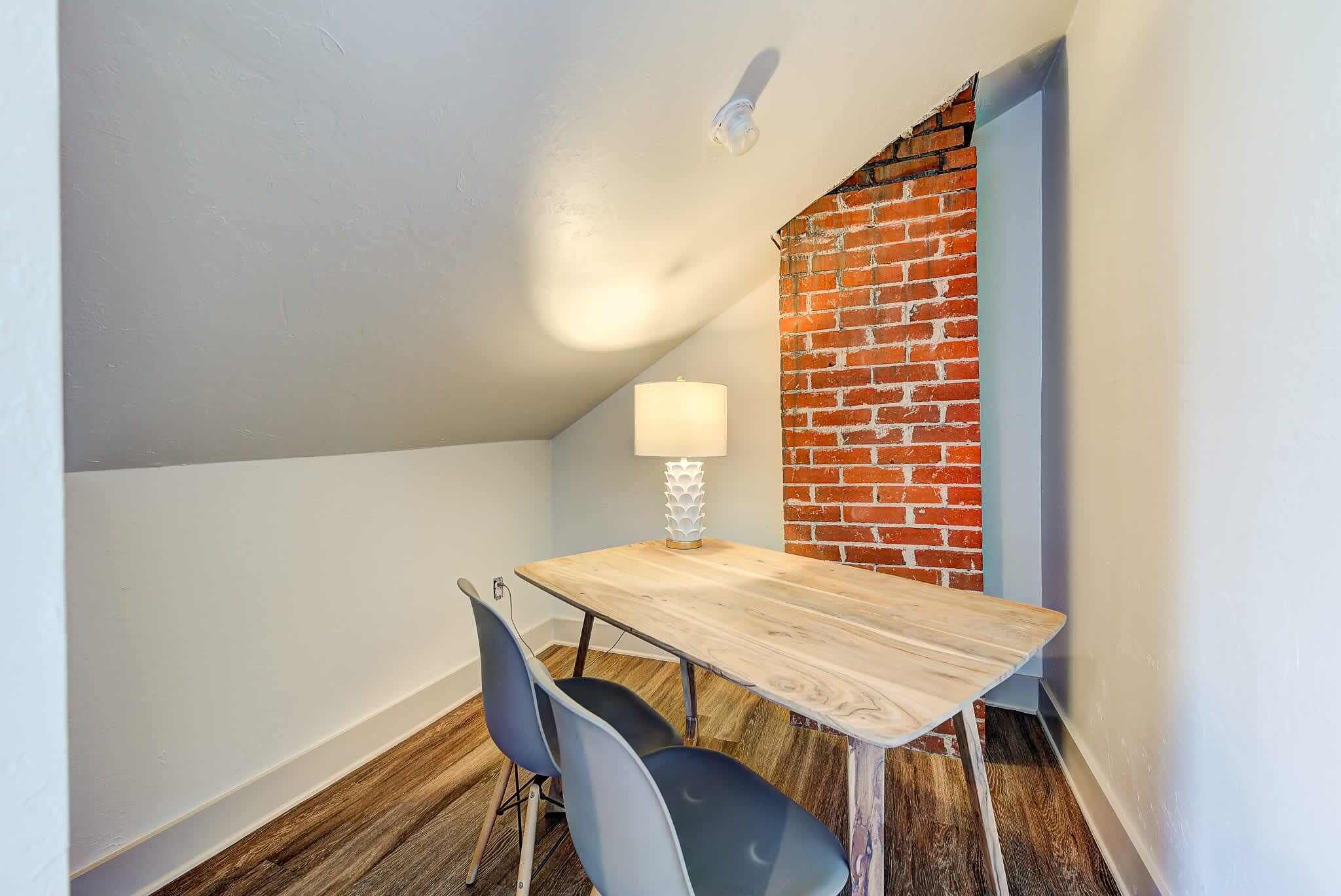 Un coin repas avec une table en bois, deux chaises, une lampe et un mur en briques.