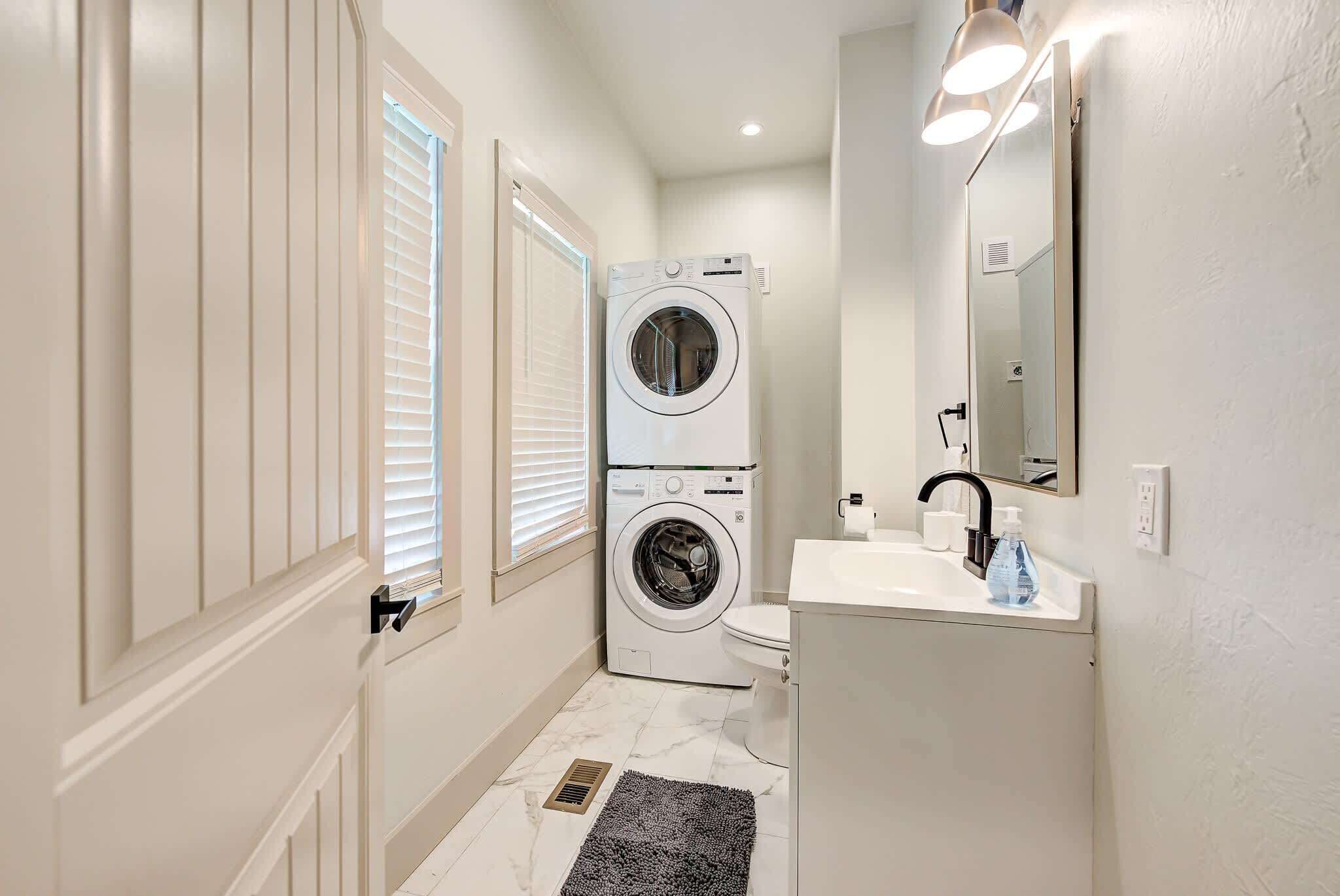 A compact bathroom with a washing machine, toilet, sink, and mirror.