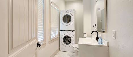 A compact bathroom with a washing machine, toilet, sink, and mirror.
