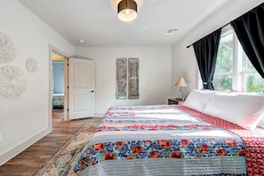 Een slaapkamer met een groot bed, een nachtkastje, een lamp en uitzicht op de natuur door een raam.