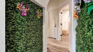 A hallway with a green wall covered in foliage, a white door, and a wooden floor.