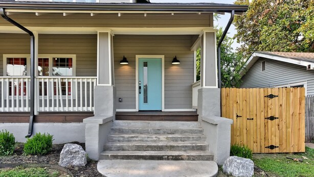 A house with a front porch, a blue door, and a wooden fence.