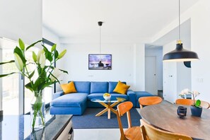 A modern living room with a blue sectional sofa, a round wooden dining table, and a large window. - Balcon del Mar (Nerja)