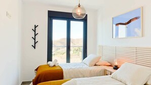 A bedroom with two beds, a large window, a wall-mounted coat rack, and a framed picture of a bird.