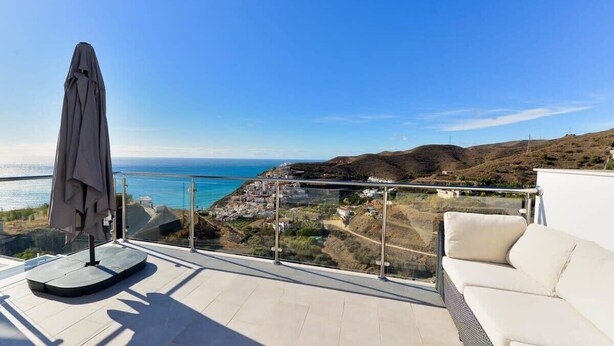A balcony with a view of the sea, a white sofa, and a covered table.